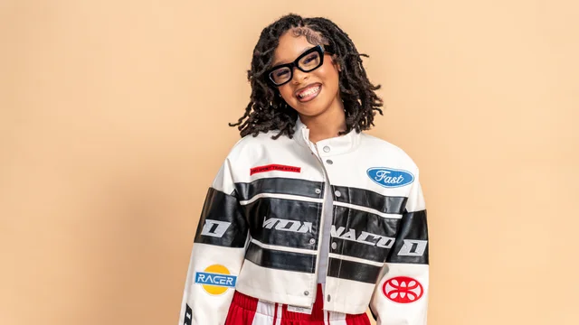 Smiling studio portrait in a motorsport jacket against a warm backdrop
