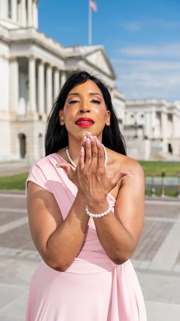 Solo portrait in a pale pink dress blowing a kiss outside the Capitol