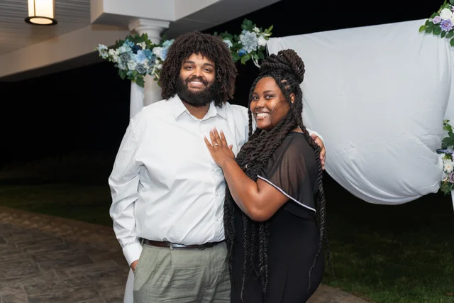 Newly engaged couple smiling together beneath a floral arch