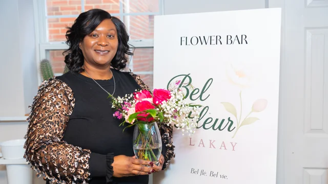 Guest holding a bouquet beside a floral workshop sign