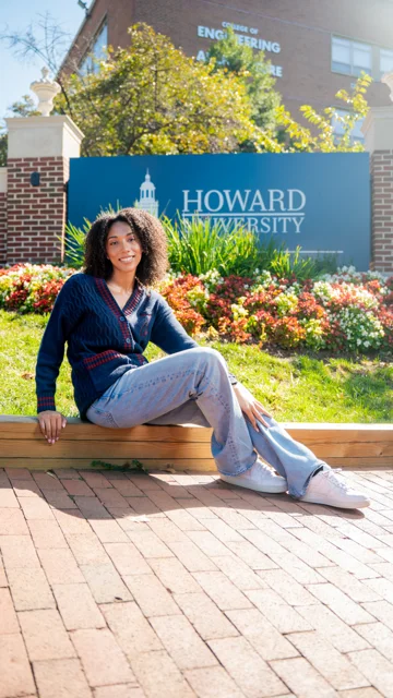 Taylor seated beside a Howard University sign for graduation portraits