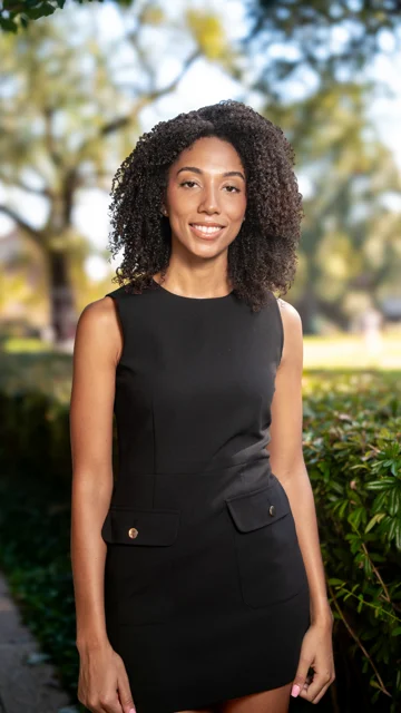 Taylor smiling in a black dress outdoors during a graduation portrait session