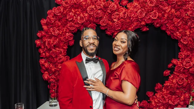 Couple in red celebrating beneath a red rose arch
