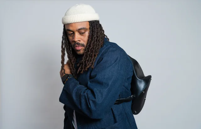Studio portrait of a man with locs and a white beanie in a navy jacket