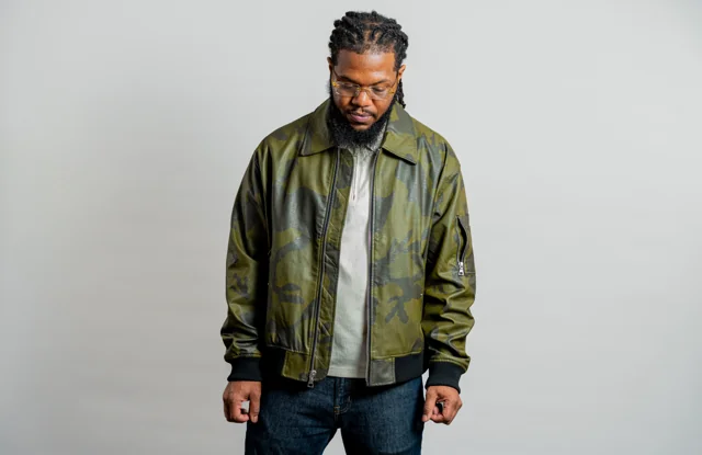 Studio portrait in a green bomber jacket against a neutral backdrop