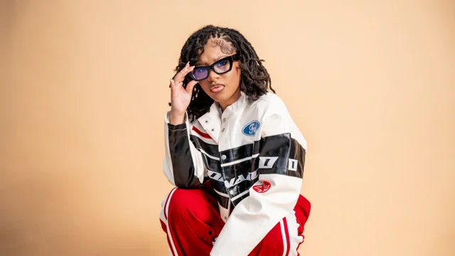 Studio portrait in a motorsport jacket and sunglasses against a warm backdrop