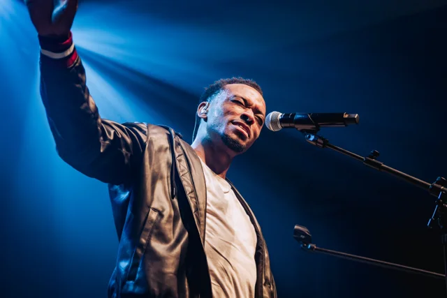 Singer reaching toward the crowd under blue concert lights