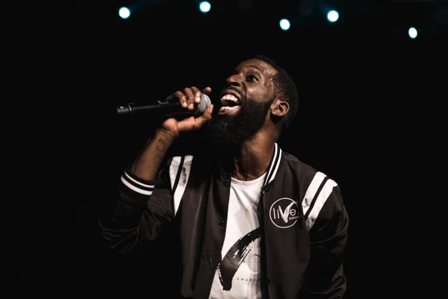 Singer performing in a varsity jacket beneath stage lights