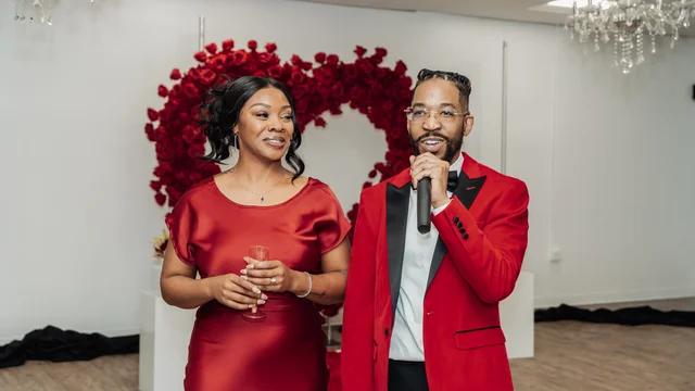 Couple addressing their guests beneath a red floral arch