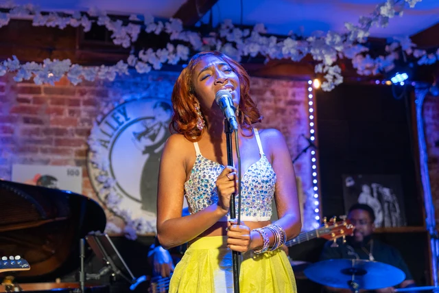 ElysCia singing with her band under blue stage lights